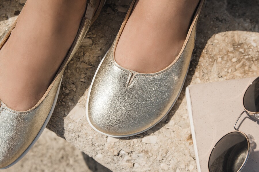 Close-up of gold metallic barefoot ballet flats on a stone in summer sun