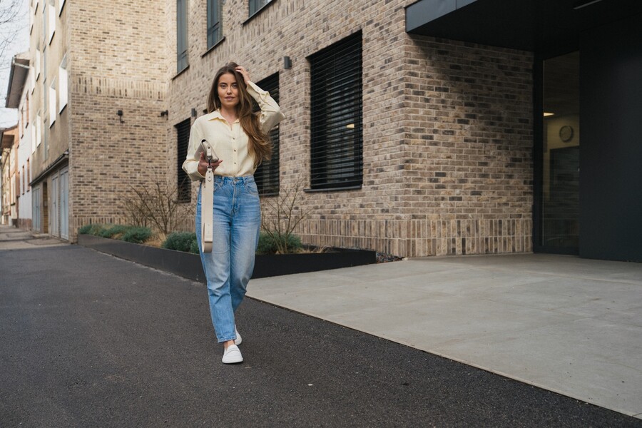 Woman in white barefoot sneakers walking down a street by a modern building
