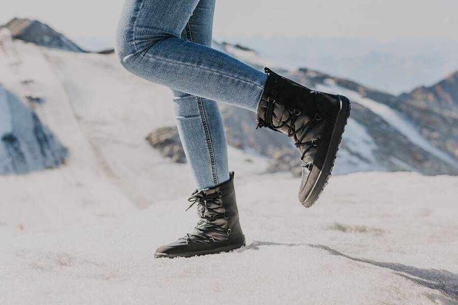 Person in black barefoot snow boots walking on snow in a mountain landscape Person in black barefoot snow boots walking on snow in a mountain landscape