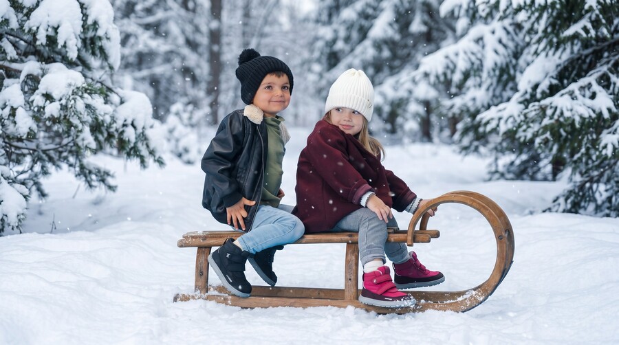 Children in winter barefoot boots sitting on a sled in a snowy landscape Children in winter barefoot boots sitting on a sled in a snowy landscape