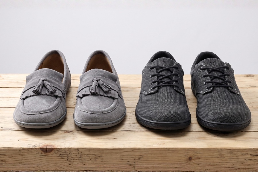 Dva páry šedých barefoot bot do práce na dřevěné desce – semišový a šněrovací model.