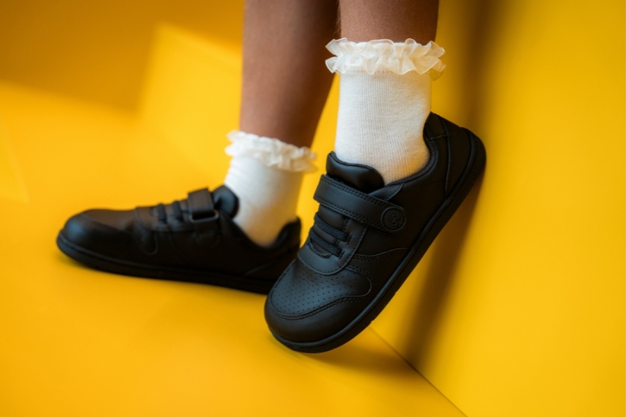 Close-up of a girl's feet in black hook-and-loop barefoot shoes for preschool on a yellow background