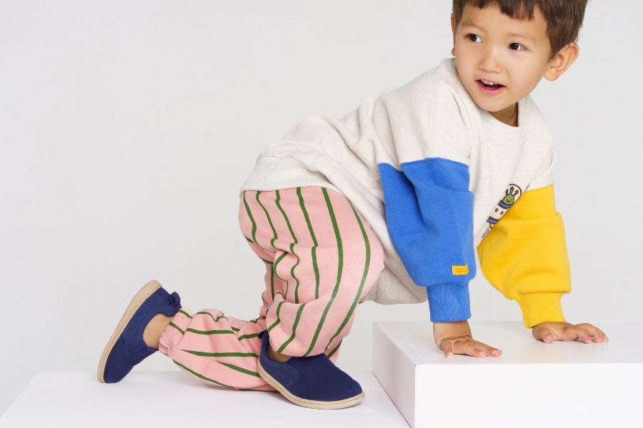 Little boy climbing a white block in navy kids' barefoot shoes with a soft flexible sole