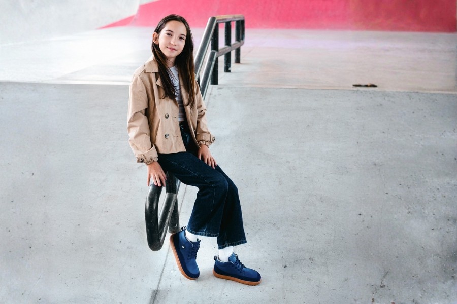 Girl sitting on a rail at a skatepark in navy kids' barefoot shoes with a gum sole, size 35–40