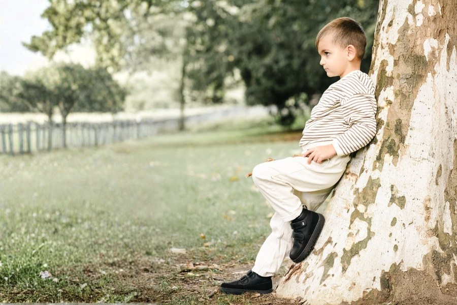 Garçon en chaussures barefoot pour enfants toute l'année noires appuyé contre un arbre dans la nature Garçon en chaussures barefoot pour enfants toute l'année noires appuyé contre un arbre dans la nature