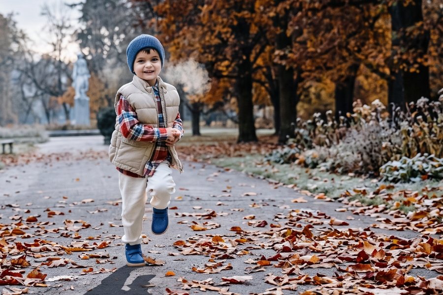 Garçon en chaussures barefoot pour enfants toute l'année bleues courant sur un chemin dans un parc en automne Garçon en chaussures barefoot pour enfants toute l'année bleues courant sur un chemin dans un parc en automne
