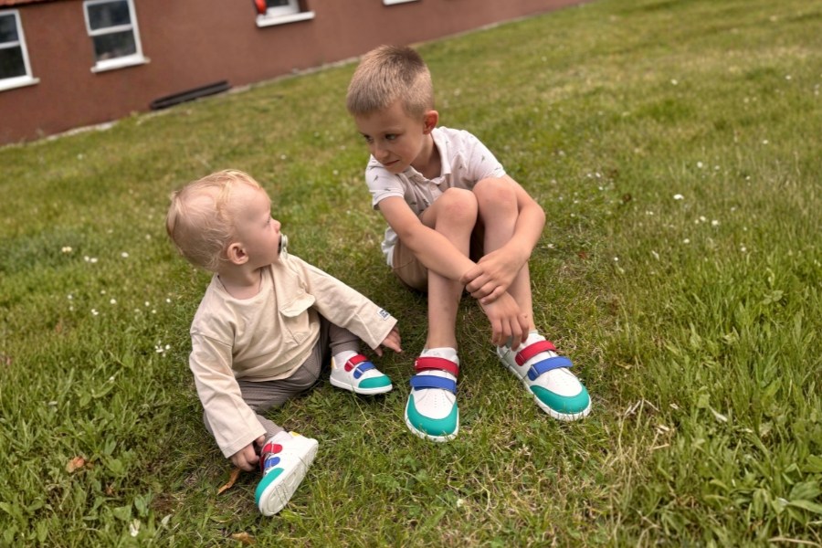 Deux enfants en chaussures barefoot pour enfants toute l'année colorées assis sur l'herbe Deux enfants en chaussures barefoot pour enfants toute l'année colorées assis sur l'herbe