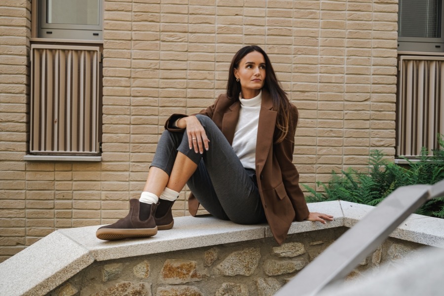 Woman in brown women's Chelsea barefoot boots sitting on a stone wall