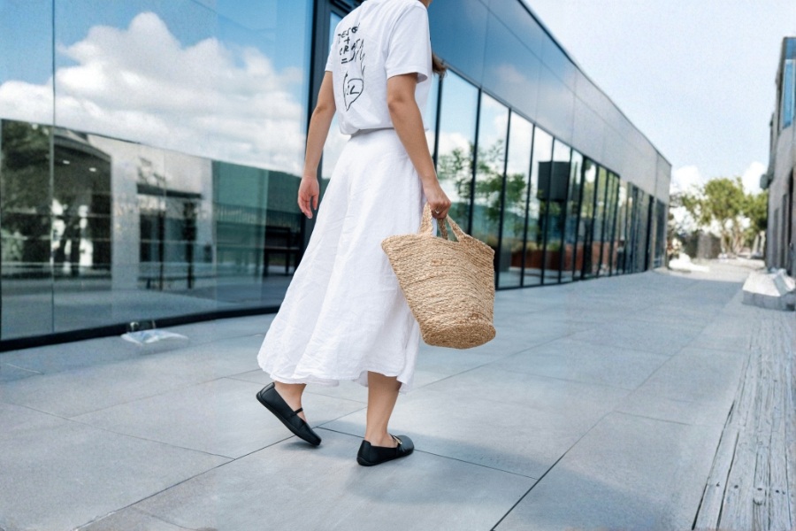 Kobieta w czarnym damskim obuwiu barefoot idzie z wiklinowym koszem przy nowoczesnym budynku Kobieta w czarnym damskim obuwiu barefoot idzie z wiklinowym koszem przy nowoczesnym budynku