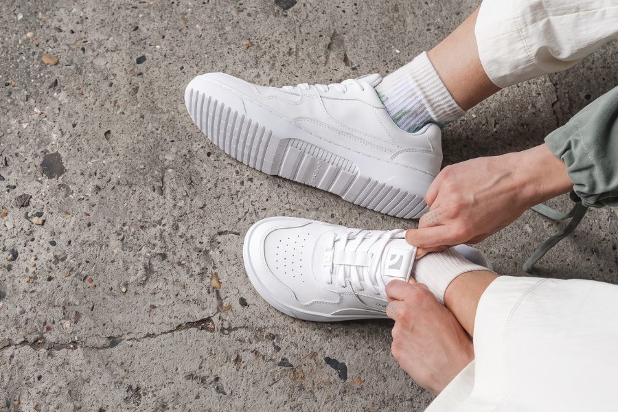 Woman lacing up white women's Barebarics sneakers on a concrete surface Woman lacing up white women's Barebarics sneakers on a concrete surface
