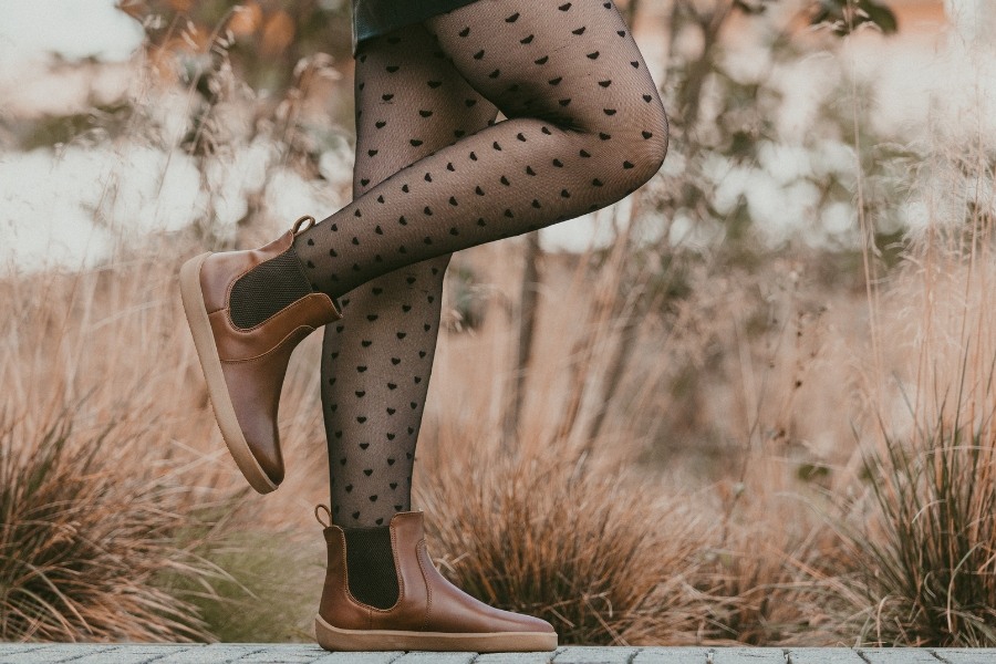 Žena v hnědých dámských barefoot kozačkách kráčí v podzimní trávě Žena v hnědých dámských barefoot kozačkách kráčí v podzimní trávě