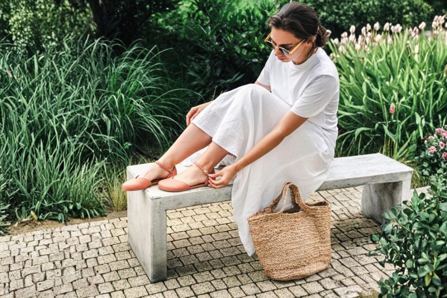 Woman putting on new orange women's barefoot shoes on a bench in a summer garden Woman putting on new orange women's barefoot shoes on a bench in a summer garden