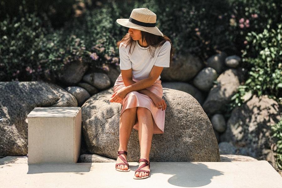 Woman in burgundy women's barefoot sandals sitting on a rock in a summer garden Woman in burgundy women's barefoot sandals sitting on a rock in a summer garden