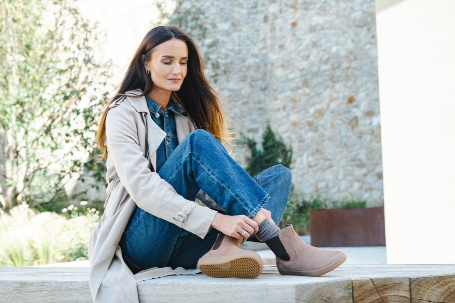 Woman putting on brown women's ankle barefoot boots on a stone wall Woman putting on brown women's ankle barefoot boots on a stone wall