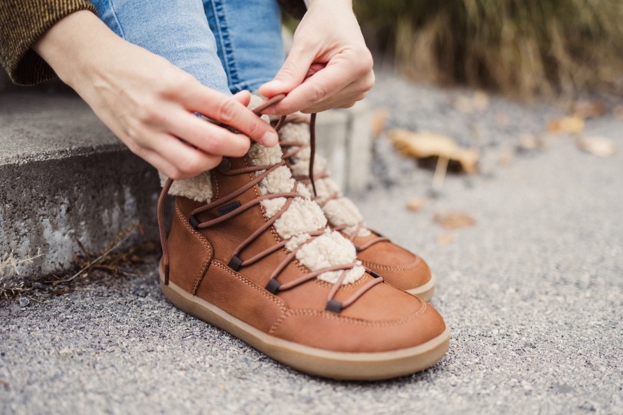 Close-up of hands lacing brown women's ankle barefoot boots with a fur trim Close-up of hands lacing brown women's ankle barefoot boots with a fur trim