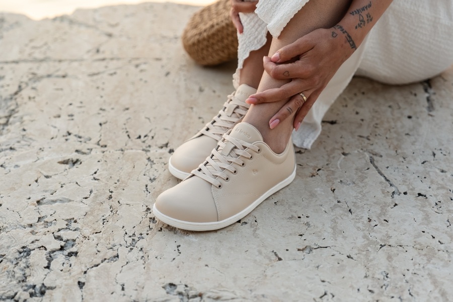 Woman lacing up beige women's spring barefoot shoes on a stone surface Woman lacing up beige women's spring barefoot shoes on a stone surface
