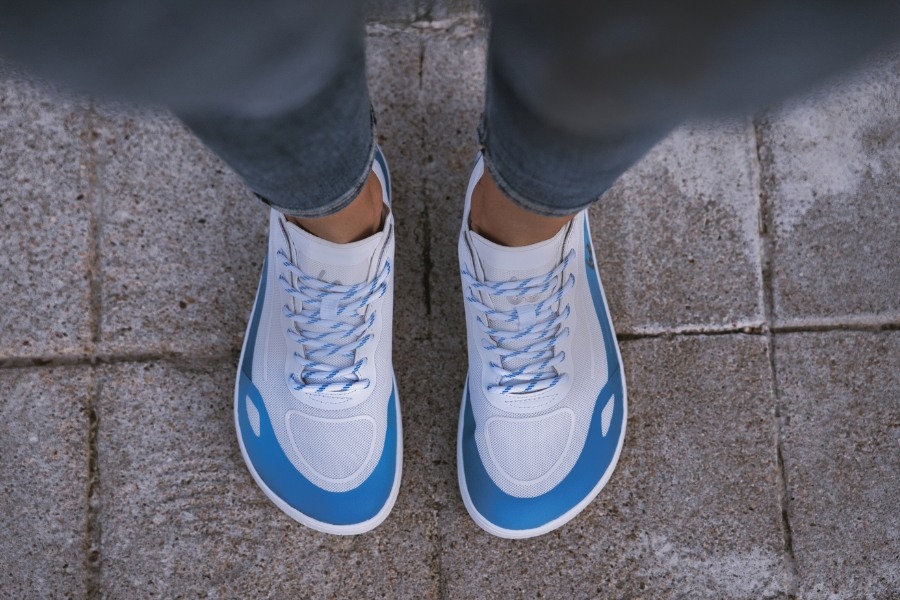 Draufsicht auf Füße in weiß-blauen Barfuß-Sommer-Damenschuhen auf einem Pflaster