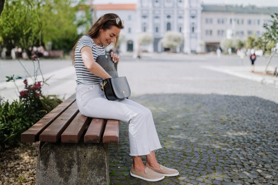 Woman in beige women's low barefoot shoes sitting on a bench in a square Woman in beige women's low barefoot shoes sitting on a bench in a square
