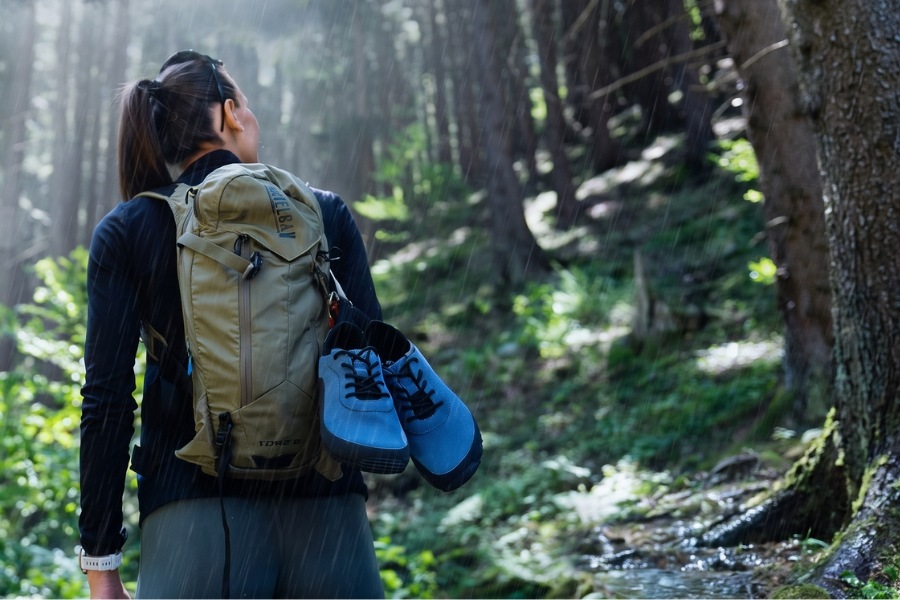 Damskie outdoorowe buty barefoot w kolorze niebieskim zawieszone na plecaku w deszczowym lesie