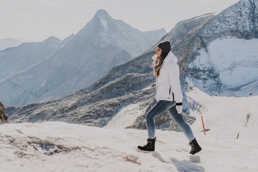 Woman in black women's winter barefoot shoes walking on a snowy mountain slope