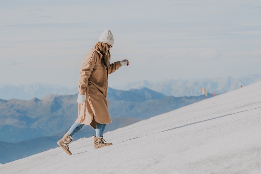 Woman in beige women's winter barefoot shoes walking on a snowy mountain slope