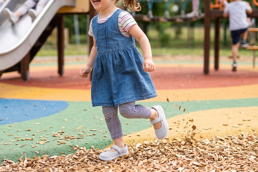 Little girl playing on a playground in light grey kids' barefoot ballet flats with an instep strap.