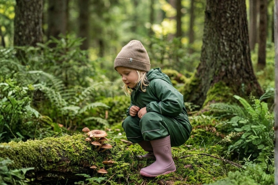 Bambina in stivali di gomma barefoot per bambini rosa osserva i funghi in un bosco
