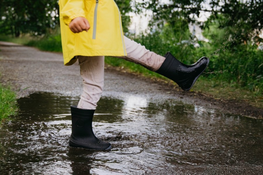 Bambino in stivali di gomma barefoot per bambini neri salta in una pozzanghera con un impermeabile giallo