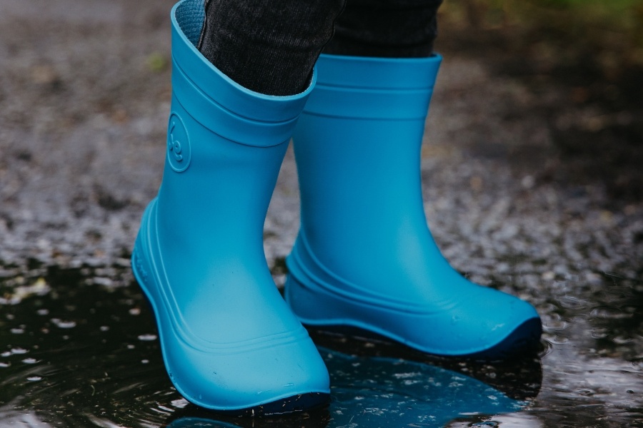 Primo piano di piedi di bambino in stivali di gomma barefoot blu in una pozzanghera