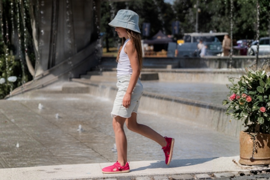 Dievča v ružových detských barefoot sandáloch kráča popri mestskej fontáne