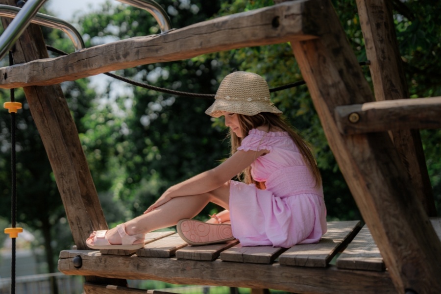 Dievča v svetloružových detských barefoot sandáloch sedí na drevenej preliezke