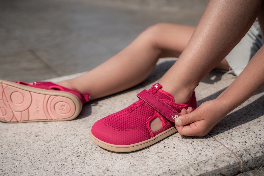 Detail detských nôh v ružových barefoot sandáloch so suchým zipsom