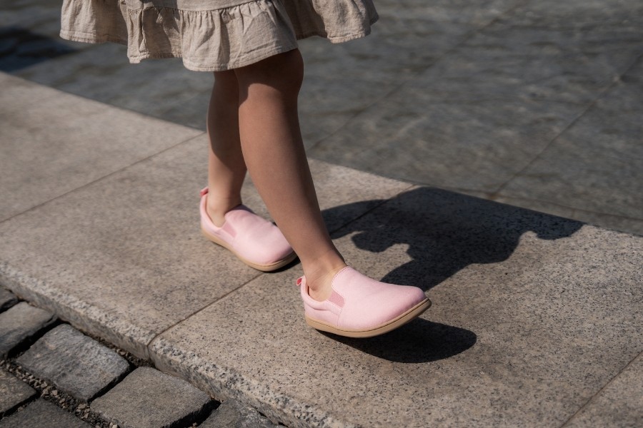 Little girl walking along a kerb in pink kids' barefoot slip-ons with a wide toe box. Little girl walking along a kerb in pink kids' barefoot slip-ons with a wide toe box.