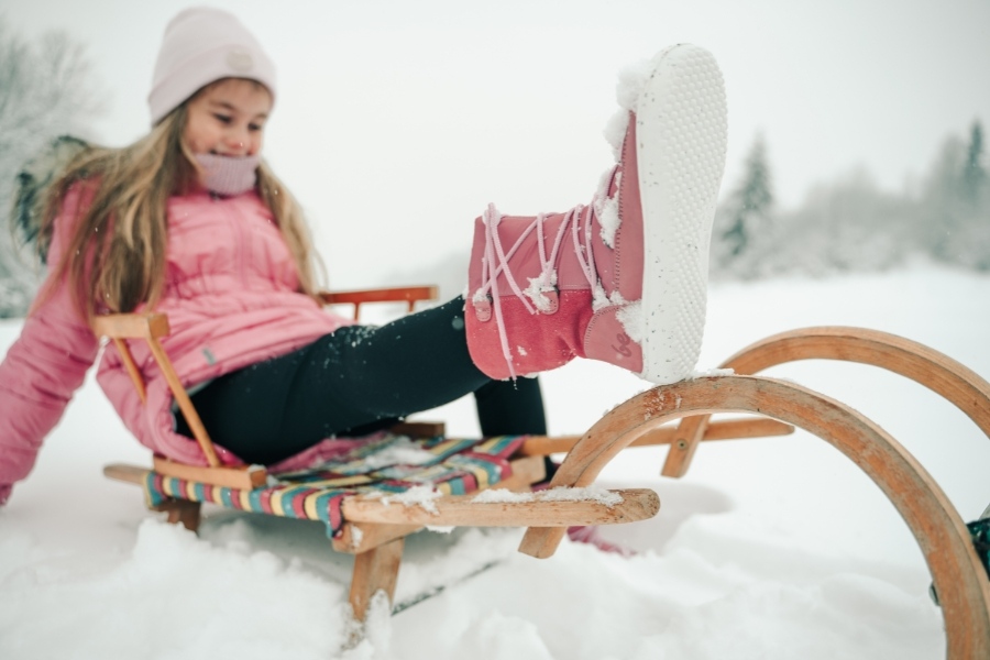 Girl in pink and white kids' barefoot snow boots sledding on the snow Girl in pink and white kids' barefoot snow boots sledding on the snow
