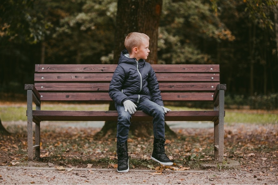 Boy in black kids' barefoot snow boots sitting on a bench in a park Boy in black kids' barefoot snow boots sitting on a bench in a park