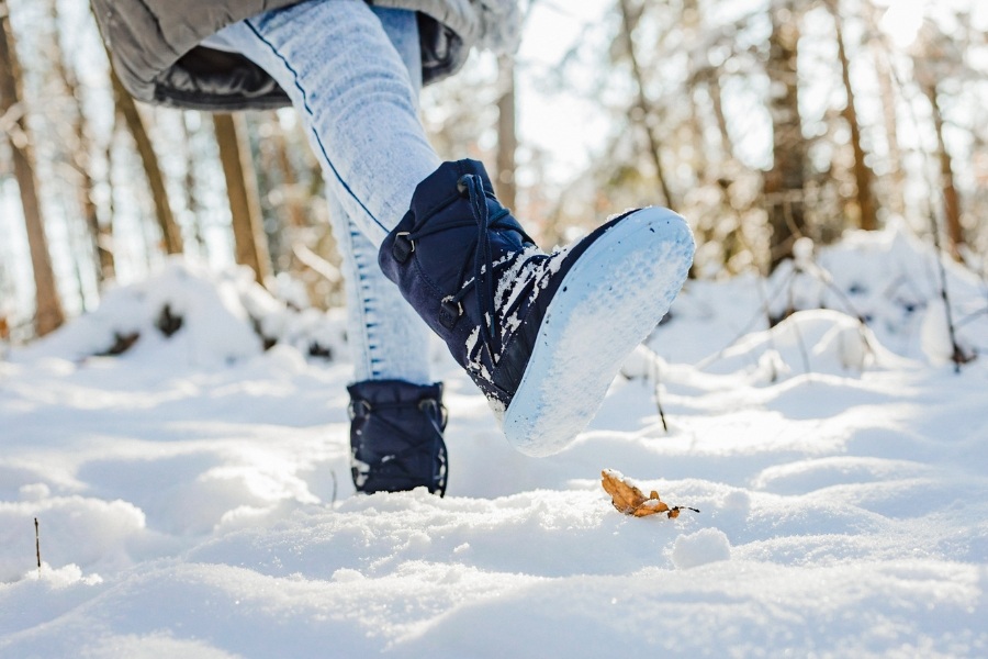 Close-up of a child's feet in navy kids' barefoot snow boots in a snowy forest Close-up of a child's feet in navy kids' barefoot snow boots in a snowy forest