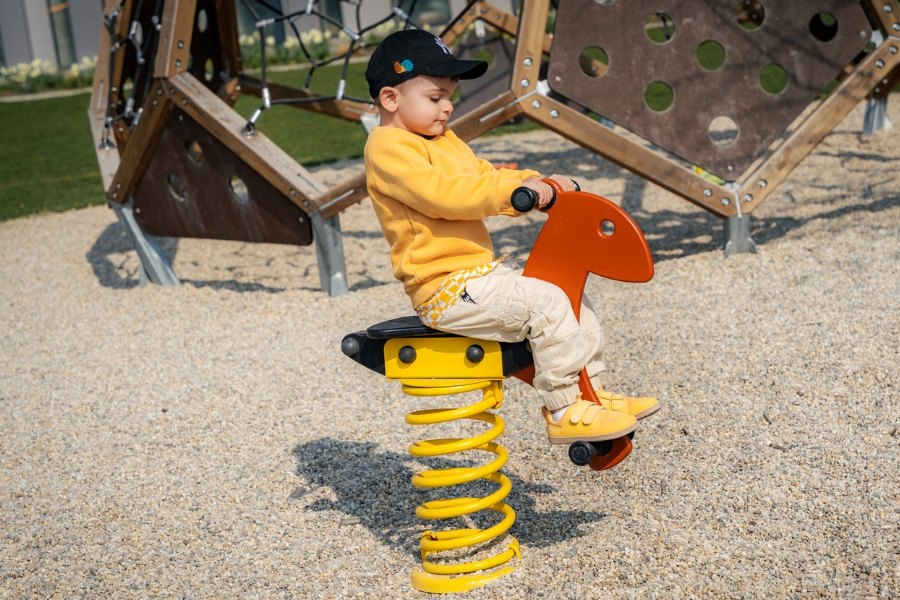 Boy in yellow kids' barefoot sneakers playing on a spring rocker at a playground