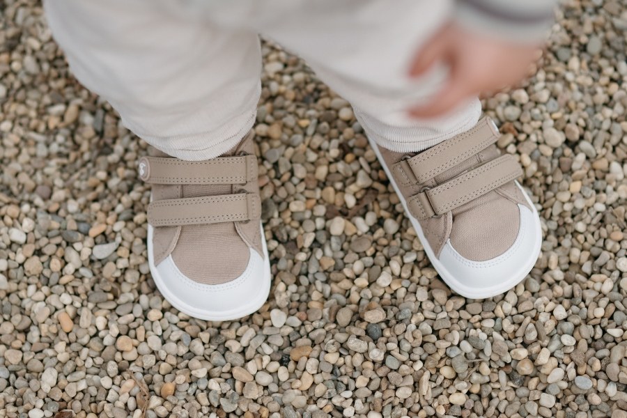 Close-up of a child's feet in beige kids' barefoot sneakers with hook-and-loop straps on gravel