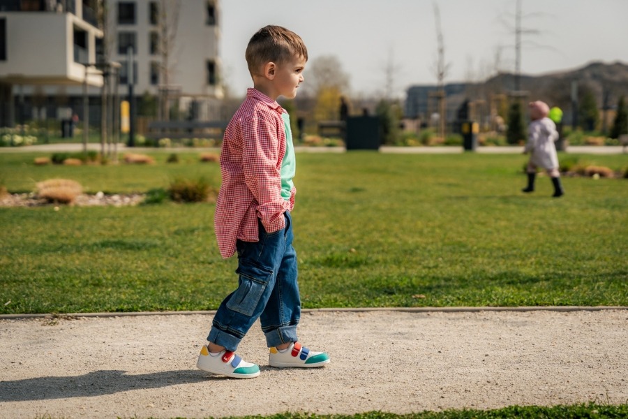 Boy walking along a park path in white everyday kids' barefoot shoes. Boy walking along a park path in white everyday kids' barefoot shoes.