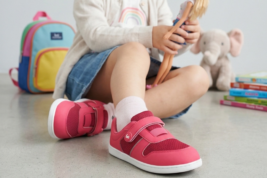 Little girl playing with a doll beside a backpack in pink everyday kids' barefoot shoes. Little girl playing with a doll beside a backpack in pink everyday kids' barefoot shoes.