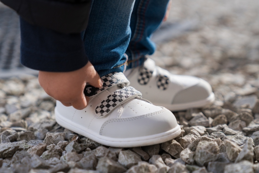 Close-up of a child's feet in white low barefoot shoes with a hook-and-loop strap on gravel