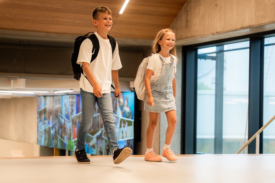 Two children in black and pink kids' low barefoot shoes walking with school backpacks