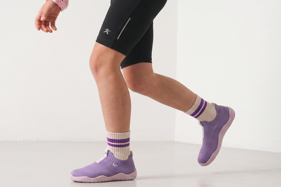 Nohy dieťaťa v behu vo fialových športových detských barefoot topánkach s ľahkou podrážkou. Nohy dieťaťa v behu vo fialových športových detských barefoot topánkach s ľahkou podrážkou.