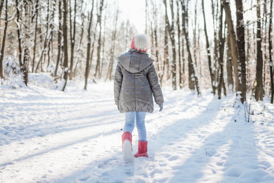 Child in red kids' winter barefoot shoes walking along a snowy forest road Child in red kids' winter barefoot shoes walking along a snowy forest road