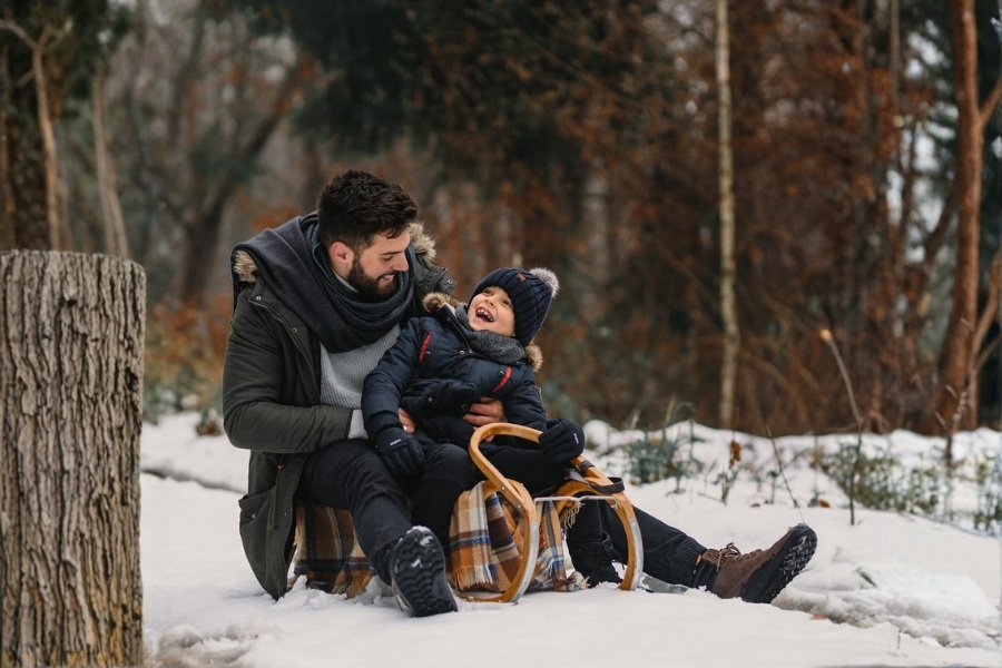 Child in dark kids' winter barefoot shoes sitting on a sled in a wintry forest Child in dark kids' winter barefoot shoes sitting on a sled in a wintry forest