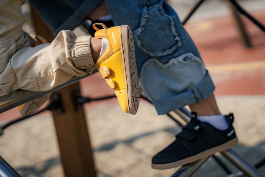 Close-up of two children's feet on climbing bars in yellow and black kids' barefoot shoes for spring.