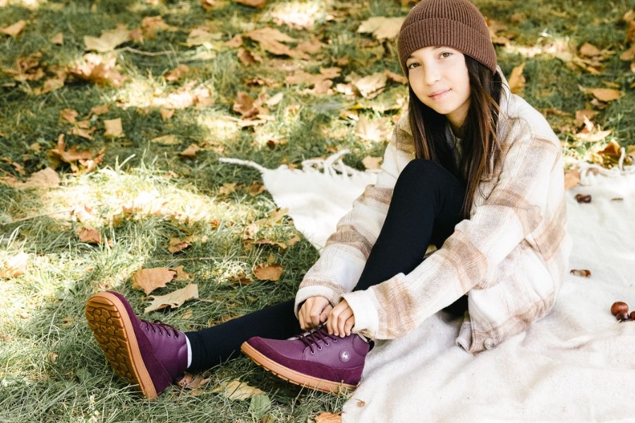 Girl sitting on a blanket among fallen leaves in burgundy kids' barefoot shoes for autumn. Girl sitting on a blanket among fallen leaves in burgundy kids' barefoot shoes for autumn.