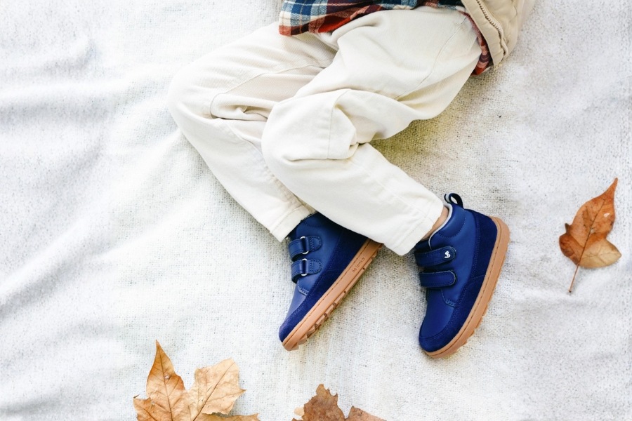 Close-up of a child's feet on a blanket in navy hook-and-loop kids' barefoot shoes for autumn. Close-up of a child's feet on a blanket in navy hook-and-loop kids' barefoot shoes for autumn.