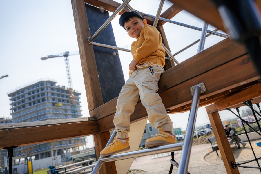 Boy climbing a playground frame in yellow kids' barefoot shoes for summer.