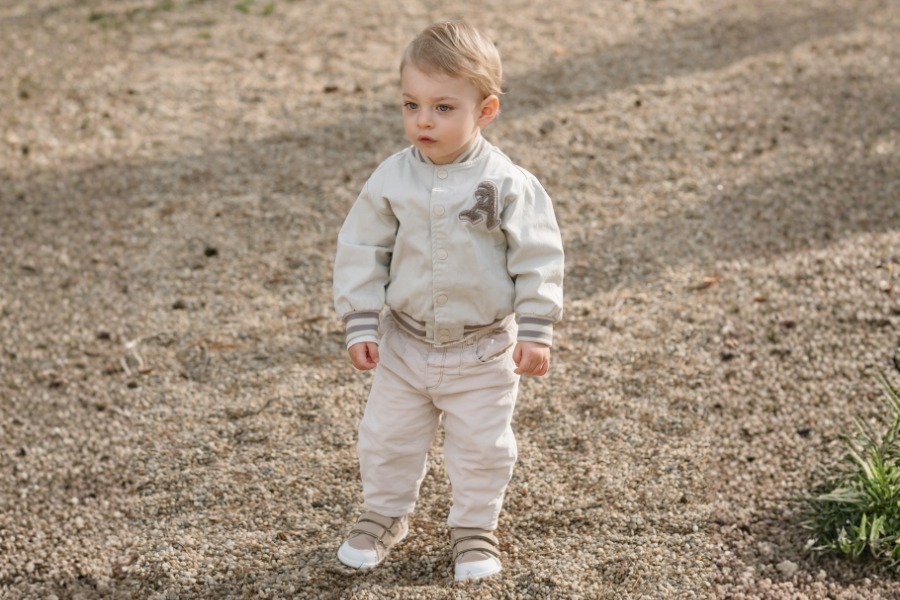 Toddler walking on gravel in beige kids' barefoot shoes for summer.